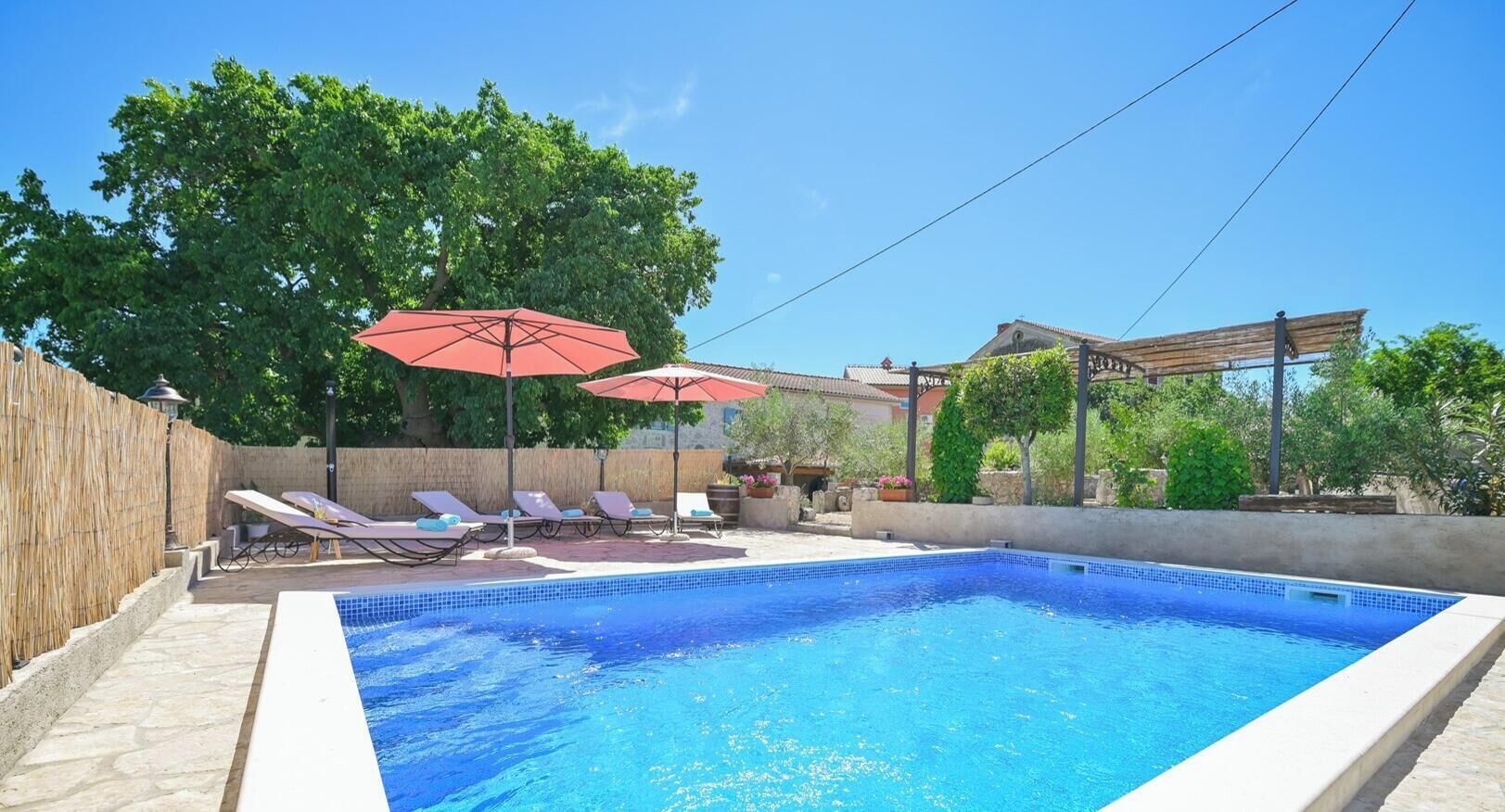 A rectangular swimming pool with a tiled edge, surrounded by lounge chairs and a red umbrella.