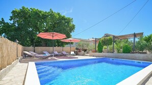 A rectangular swimming pool with a tiled edge, surrounded by lounge chairs and a red umbrella. - Beautiful Villa Bogovski Dvori**** with a rustic touch on Krk (Malinska)