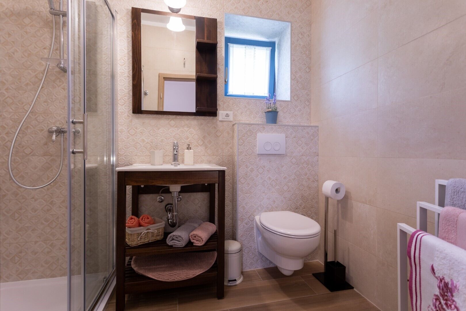 A bathroom with a glass shower enclosure, a sink with a mirror above, a toilet, and a towel rack with towels.