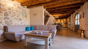 A cozy living room with a stone wall, wooden ceiling beams, a sofa, and a coffee table. - Beautiful Villa Bogovski Dvori**** with a rustic touch on Krk (Malinska)