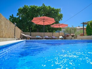 En swimmingpool med blå kakelplattor, solstolar och röda parasoller.