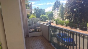 A balcony with a tiled floor, a metal railing, and a view of a street with cars and buildings.