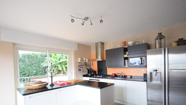 A modern kitchen with a central island, stainless steel appliances, and a view of greenery outside.