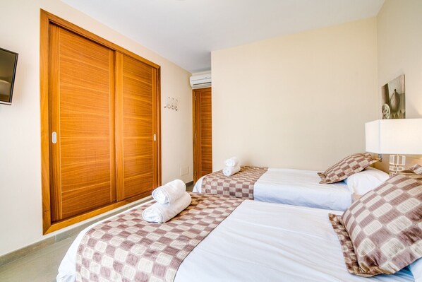 Een hotelkamer met twee bedden, een houten garderobe, een airconditioning en een televisie aan de muur.