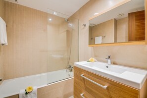 A modern bathroom with a glass-enclosed shower, a white bathtub, and a wooden vanity with a mirror. - Apartment Alcudia Portobello with seaview (Puerto de Alcudia)
