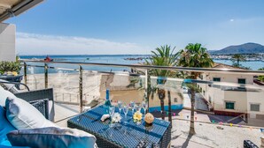 A balcony with a view of the sea, a table set with glasses and flowers, and a palm tree. - Apartment Alcudia Portobello with seaview (Puerto de Alcudia)