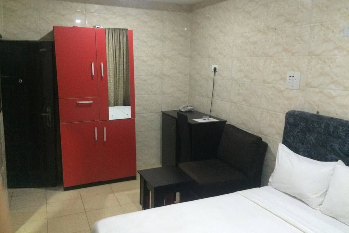 Une chambre d’hôtel avec un lit, une armoire rouge, une petite table et une table de chevet.