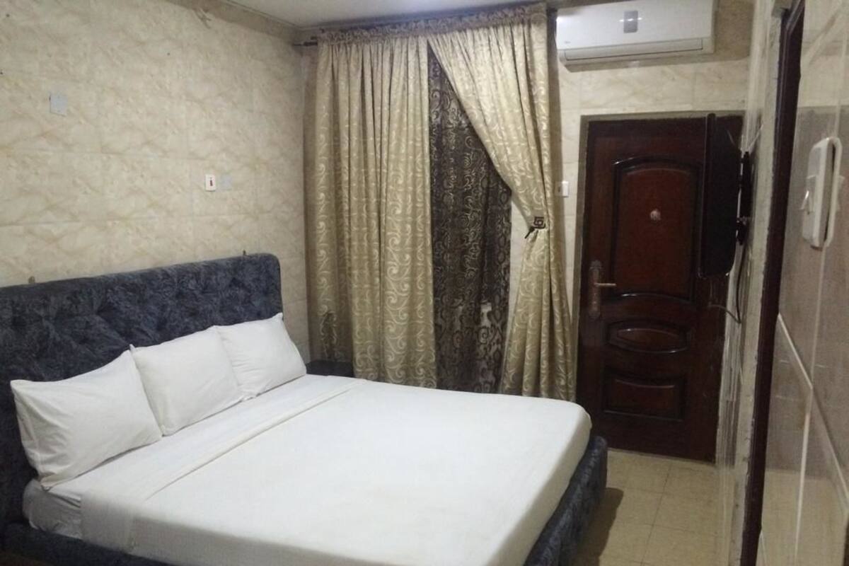 Une chambre à coucher avec un lit, des rideaux, une porte en bois et un appareil de climatisation.