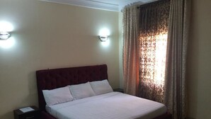 A neatly made bed in a room with a headboard, a bedside table, and a lamp. - Valton Hotels Abuja (Abuja)