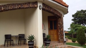 A covered outdoor seating area with two chairs and a table, a potted plant, and a stone archway. - Kolping Hotel Masindi (Masindi)