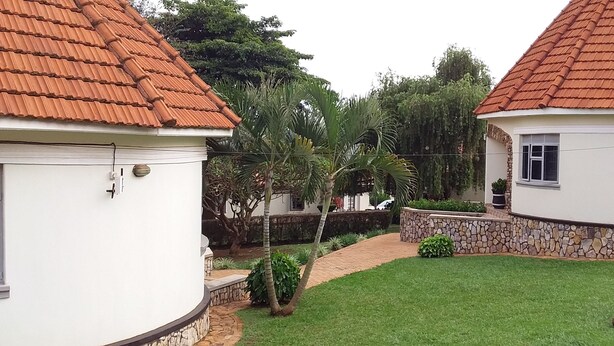 A residential area with two houses, each with a red-tiled roof and white walls. There is a paved pathway between the houses, surrounded by greenery and a small garden area. - Kolping Hotel Masindi (Masindi)