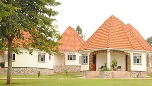 A building with a symmetrical design, featuring a central covered area with columns and a stone base. - Kolping Hotel Masindi (Masindi)