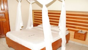 A wooden bed with a canopy, a bedside table, and a nightstand. - Kolping Hotel Masindi (Masindi)