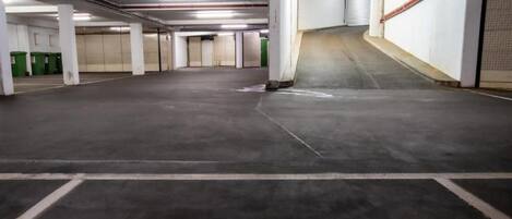 Un estacionamiento vacío con pisos de concreto, pilares blancos y contenedores de basura verdes.