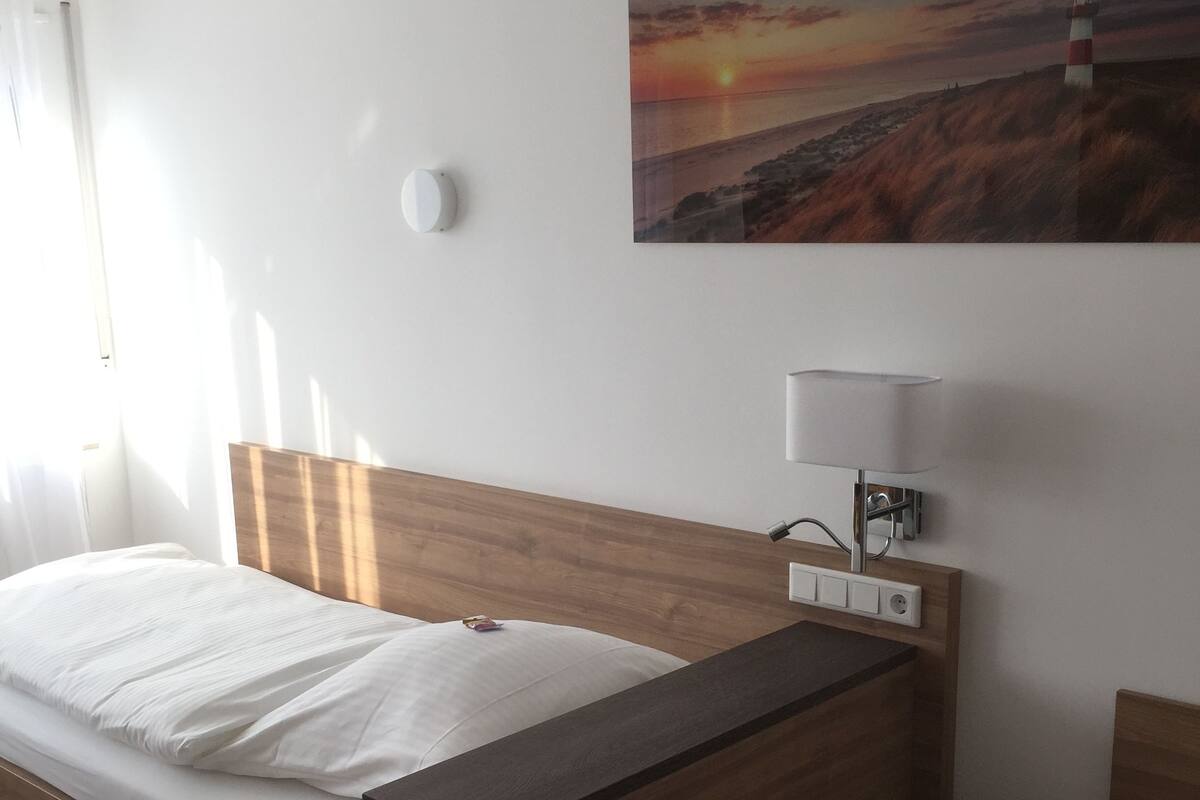 Ett hotellrum med en säng i trä, ett nattduksbord med en lampa och en tavla som föreställer en solnedgång på väggen.