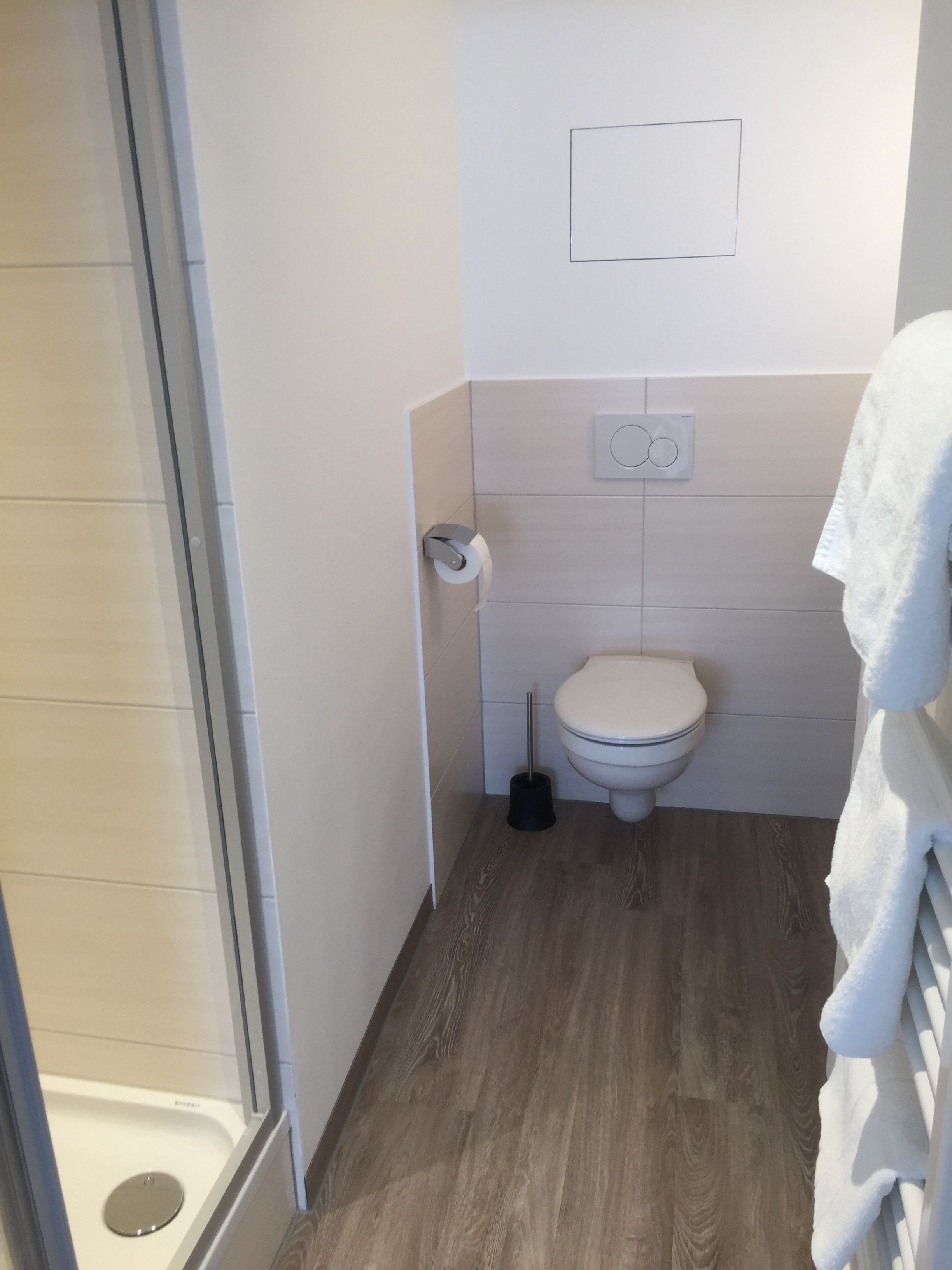 Une petite salle de bain comprenant des toilettes, un porte-rouleau de papier toilette, une ventouse et un porte-serviettes.