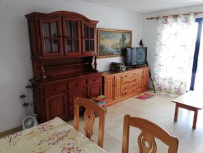 Una habitación con un armario de madera, un televisor encima y un cuadro en la pared, además de una cortina con estampado floral.