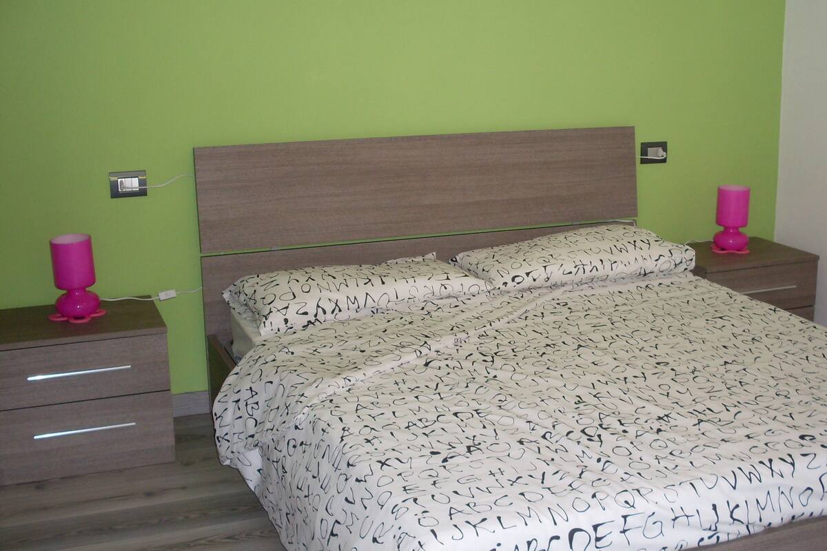 A bedroom with a bed, two nightstands, a lamp, and a drawer unit.