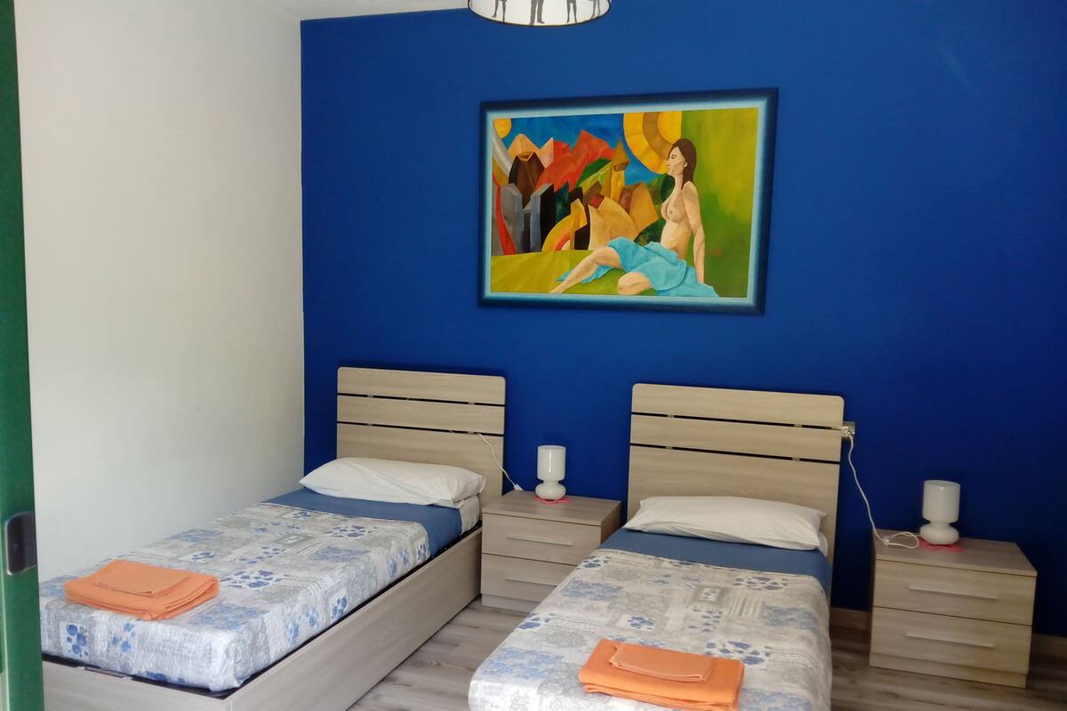 A bedroom with two beds, a painting on the wall, and a nightstand with a lamp.