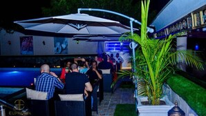 An outdoor bar area with a pool, umbrellas, and people socializing. - Commodore Hotel Abuja (Abuja)