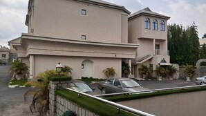 A multi-story building with a flat roof, a balcony on the second floor, and a parking area with cars. - Commodore Hotel Abuja (Abuja)