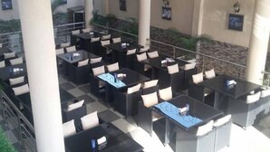 An outdoor seating area with tables and chairs arranged in rows, surrounded by columns and a stone wall. - Commodore Hotel Abuja (Abuja)