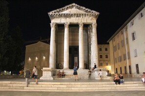 Ein klassizistisches Gebäude mit Säulen, einer zentralen Treppe und einer umgebenden Stadtlandschaft bei Nacht.