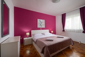 Ein Hotelzimmer mit Bett, Nachttischen, einem Spiegel, einem Fenster mit Vorhängen und einer Wand mit einem Gemälde.