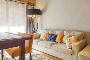 Sala de estar com sofá bege, mesa de jantar de madeira e abajur preto.