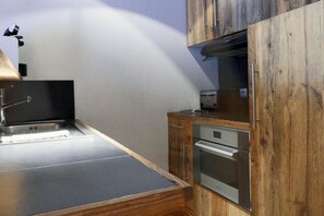 A kitchenette with a stainless steel sink, wooden cabinets, and a built-in oven.