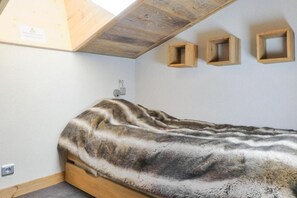A bedroom with a sloped ceiling, a bed with a patterned blanket, and three wooden wall shelves.