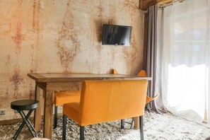A room with a wooden table, two chairs, a television mounted on the wall, and a window with curtains.