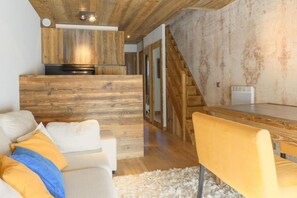 A modern interior with a wooden ceiling, a kitchen area, a staircase, and a seating area with a sofa and a chair.