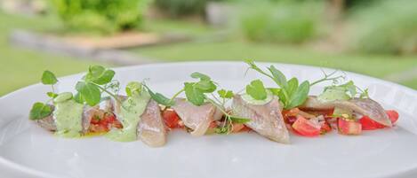 A white plate with a seafood dish garnished with herbs, set against a blurred green background.