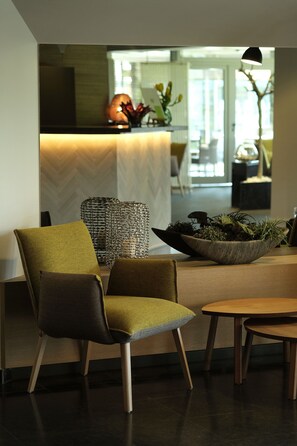 A modern dining area with a wooden table, two upholstered chairs, a woven side table, and a bowl of plants.