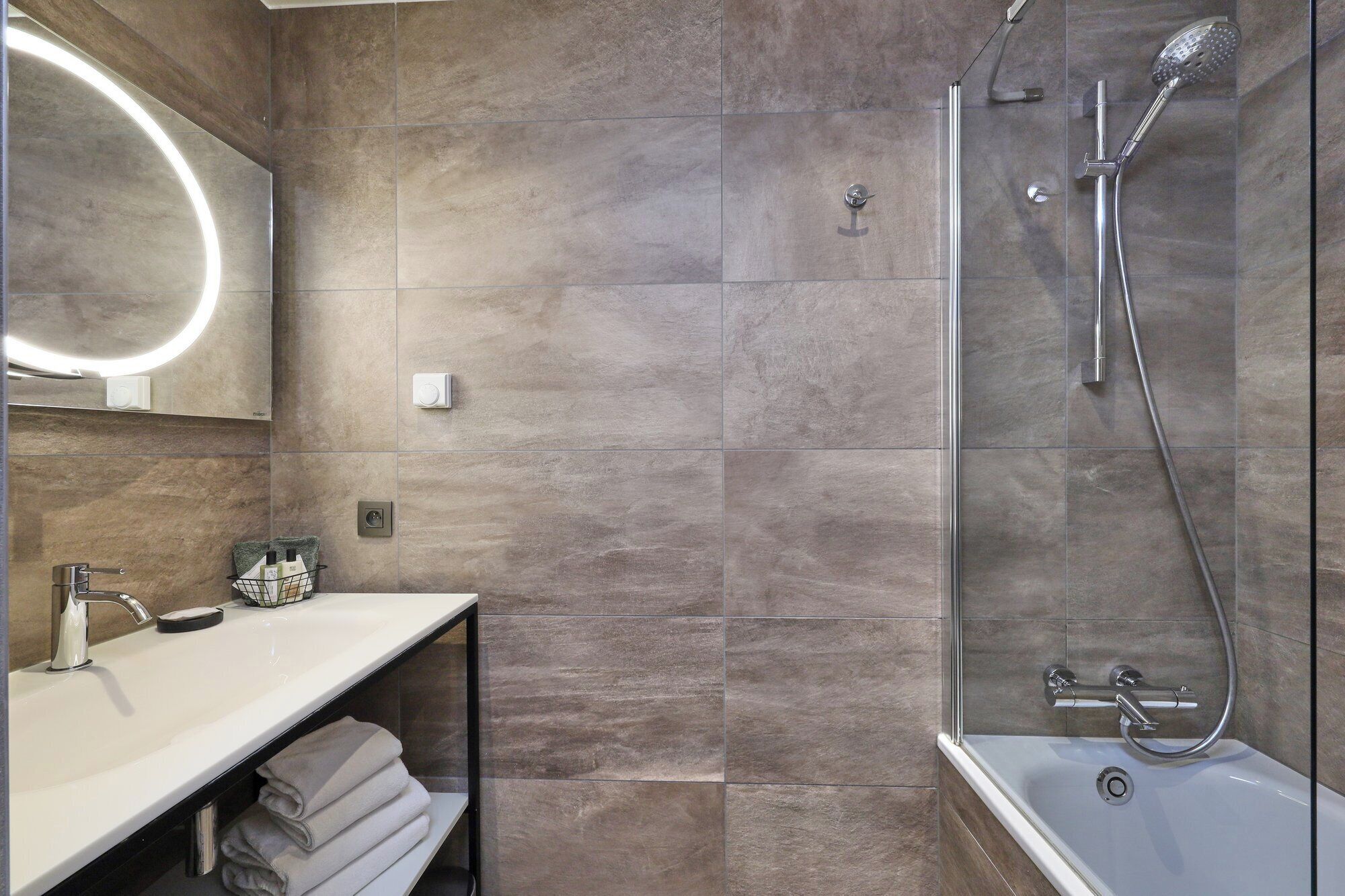 A modern bathroom with a vanity, a mirror, a shower with a handheld showerhead, and a bathtub.