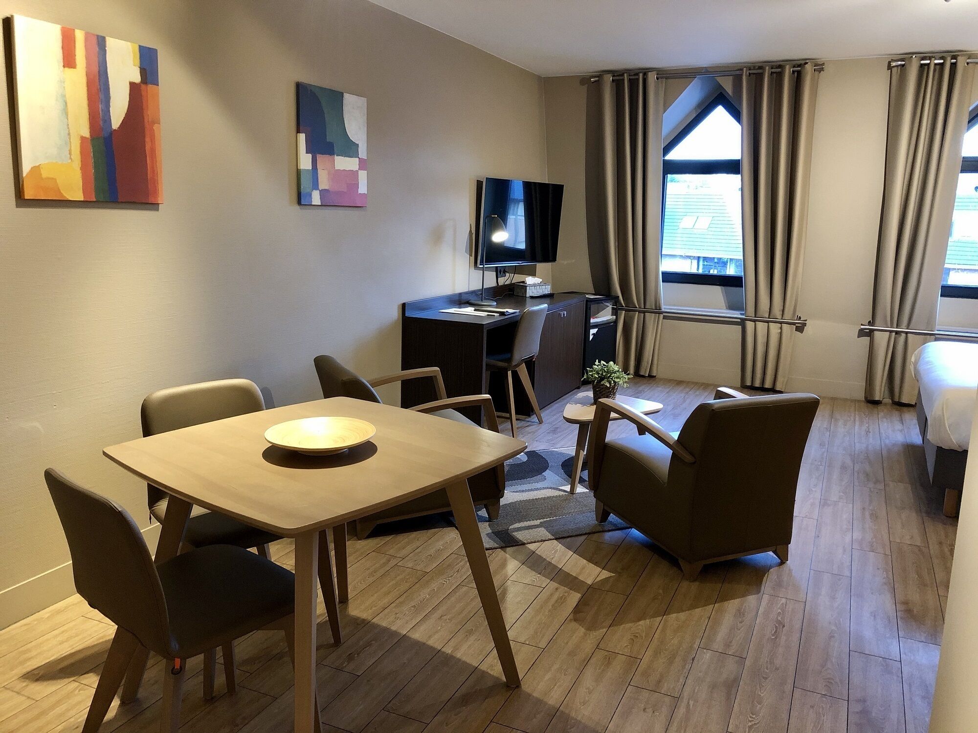 Habitación de hotel con comedor, escritorio con computadora, televisor y cama.