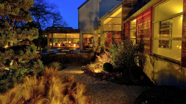 Une maison moderne dotée d’un patio bien éclairé, de grandes fenêtres et d’une allée gravillonnée.