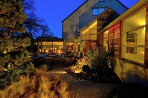 A modern house with a well-lit patio area, large windows, and a gravel driveway.