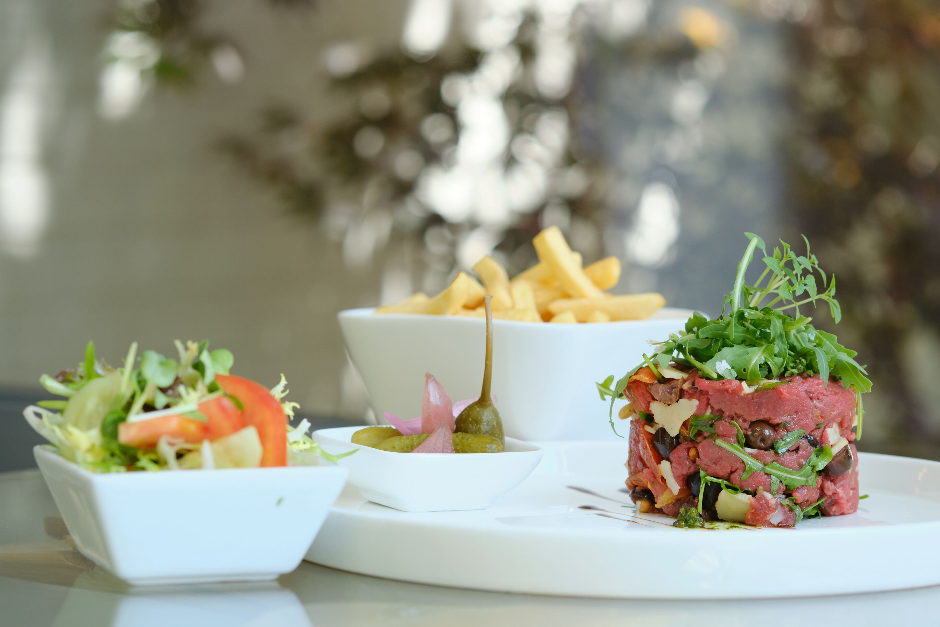 Diverse gerechten, waaronder een salade, een portie friet en een vleesgerecht, geserveerd op een wit bord.