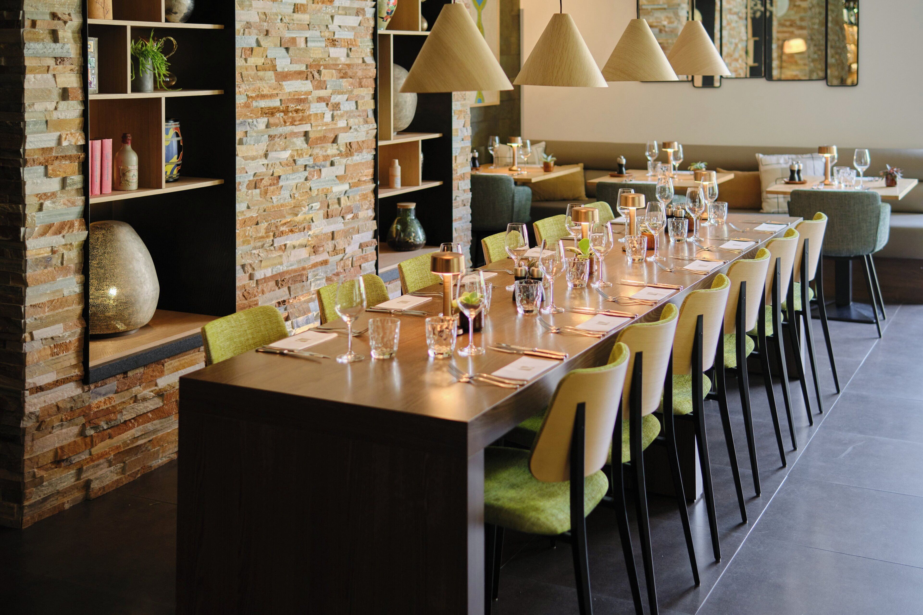 A long dining table set with chairs, a brick wall, and shelves with decorative items.