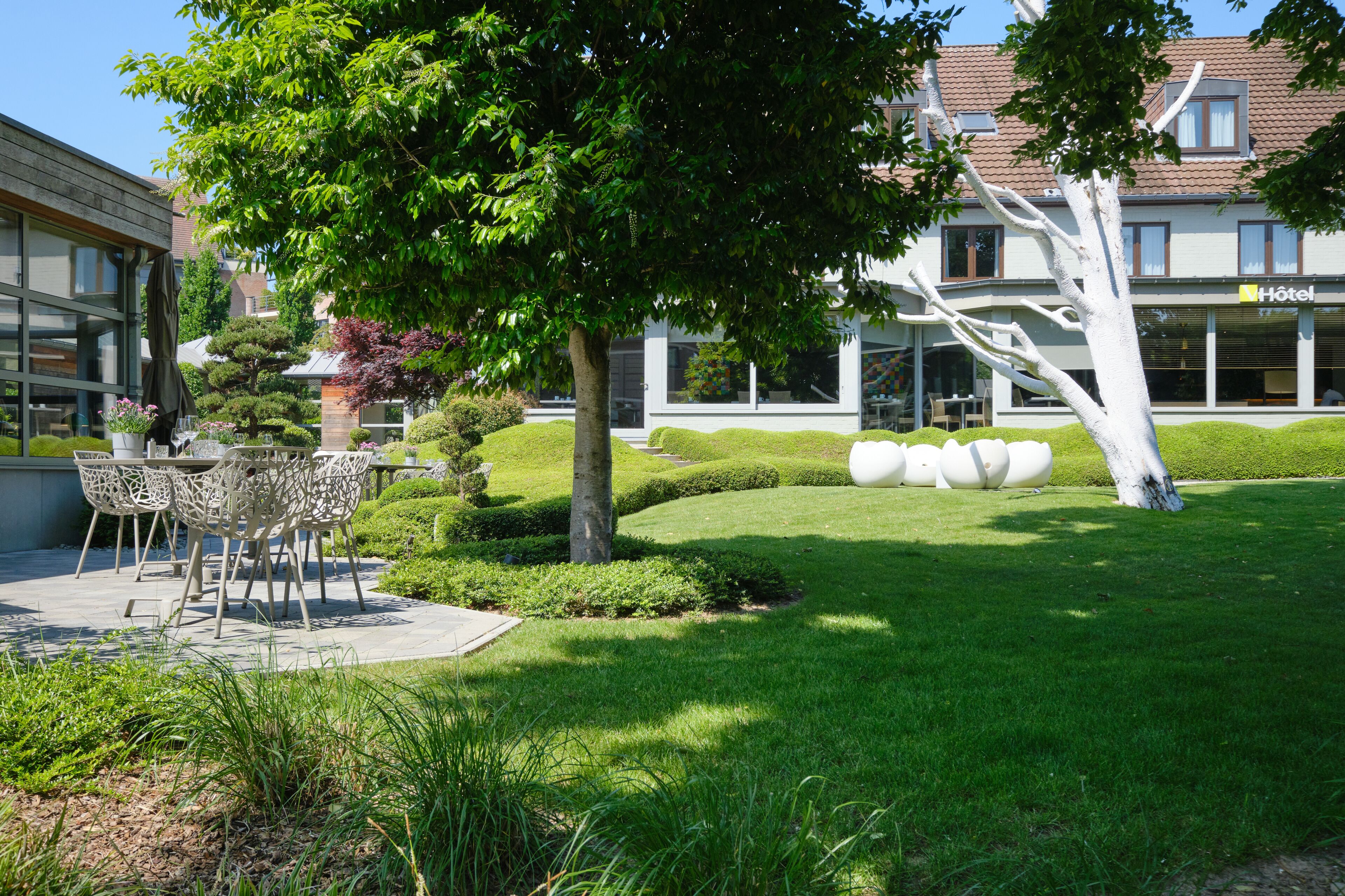 A hotel with a well-maintained garden, outdoor seating area, and a visible hotel sign.