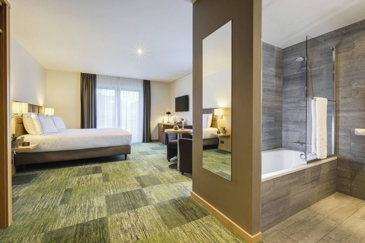A hotel room with a bed, a desk, a chair, a TV, a bathroom with a bathtub, and a shower.