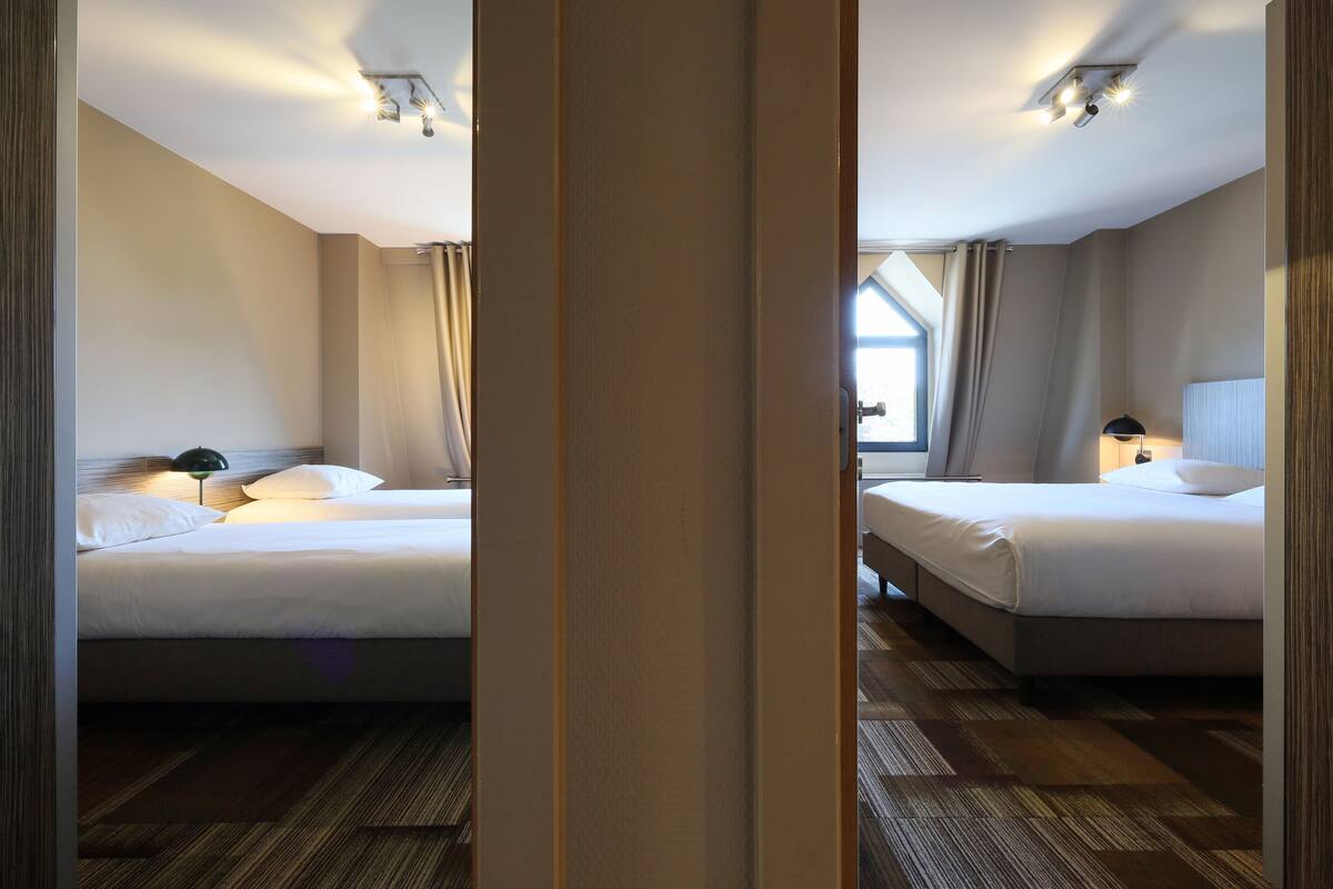A hotel room with two beds, a window with curtains, and a ceiling light fixture.
