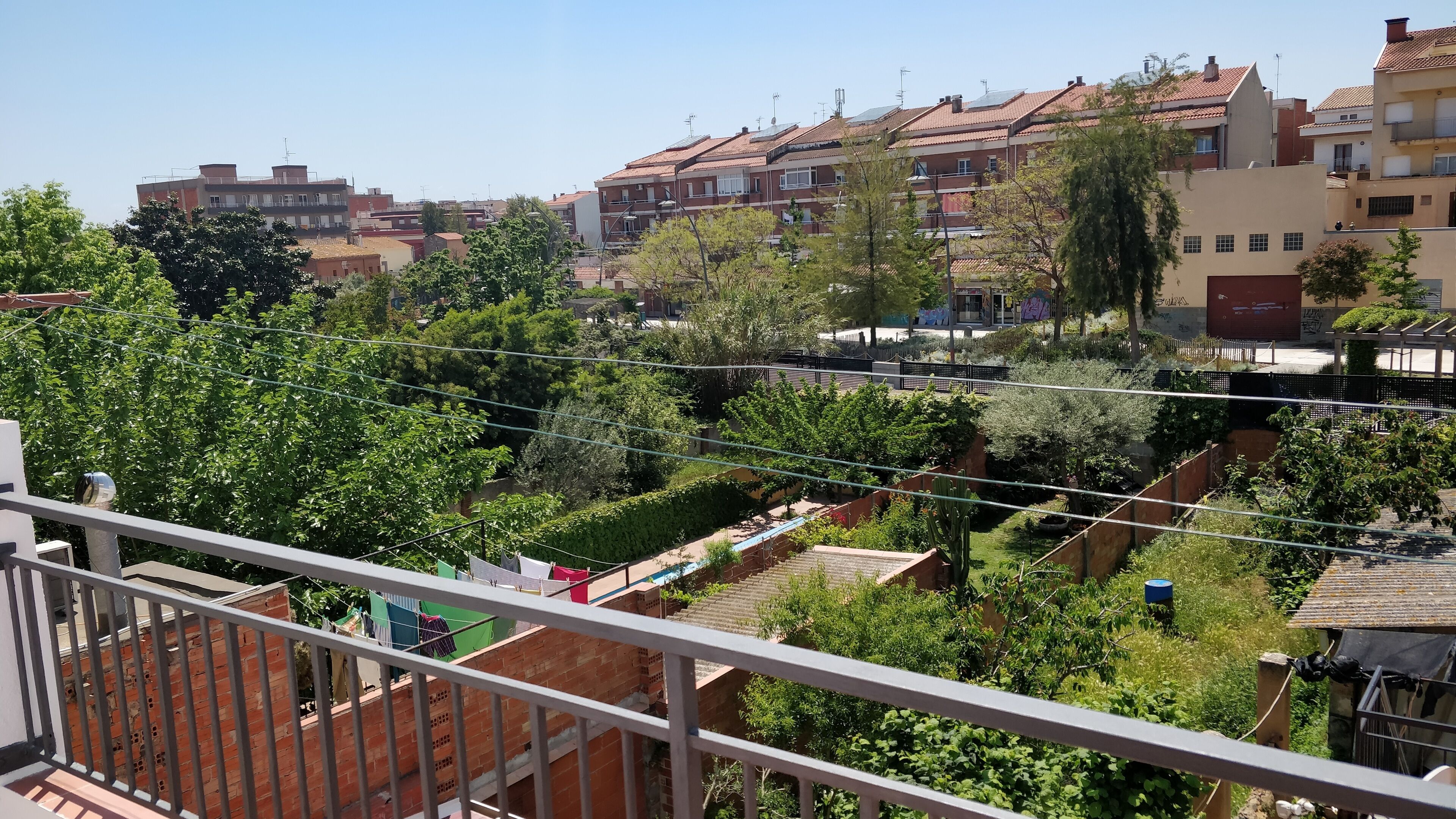 A residential area with multiple buildings, a balcony with clothes drying, and a garden with various plants.