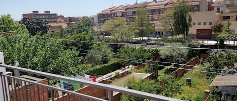 A residential area with multiple buildings, a balcony with clothes drying, and a garden with various plants.