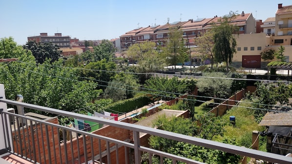 A residential area with multiple buildings, a balcony with clothes drying, and a garden with various plants.