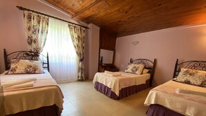 Habitación con tres camas, techo de madera y ventana con cortinas florales.