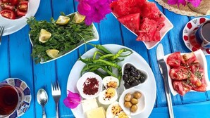 Una mesa con diversos platos, entre ellos sandía, huevos, aceitunas y una fuente de verduras, sobre una superficie de madera azul.