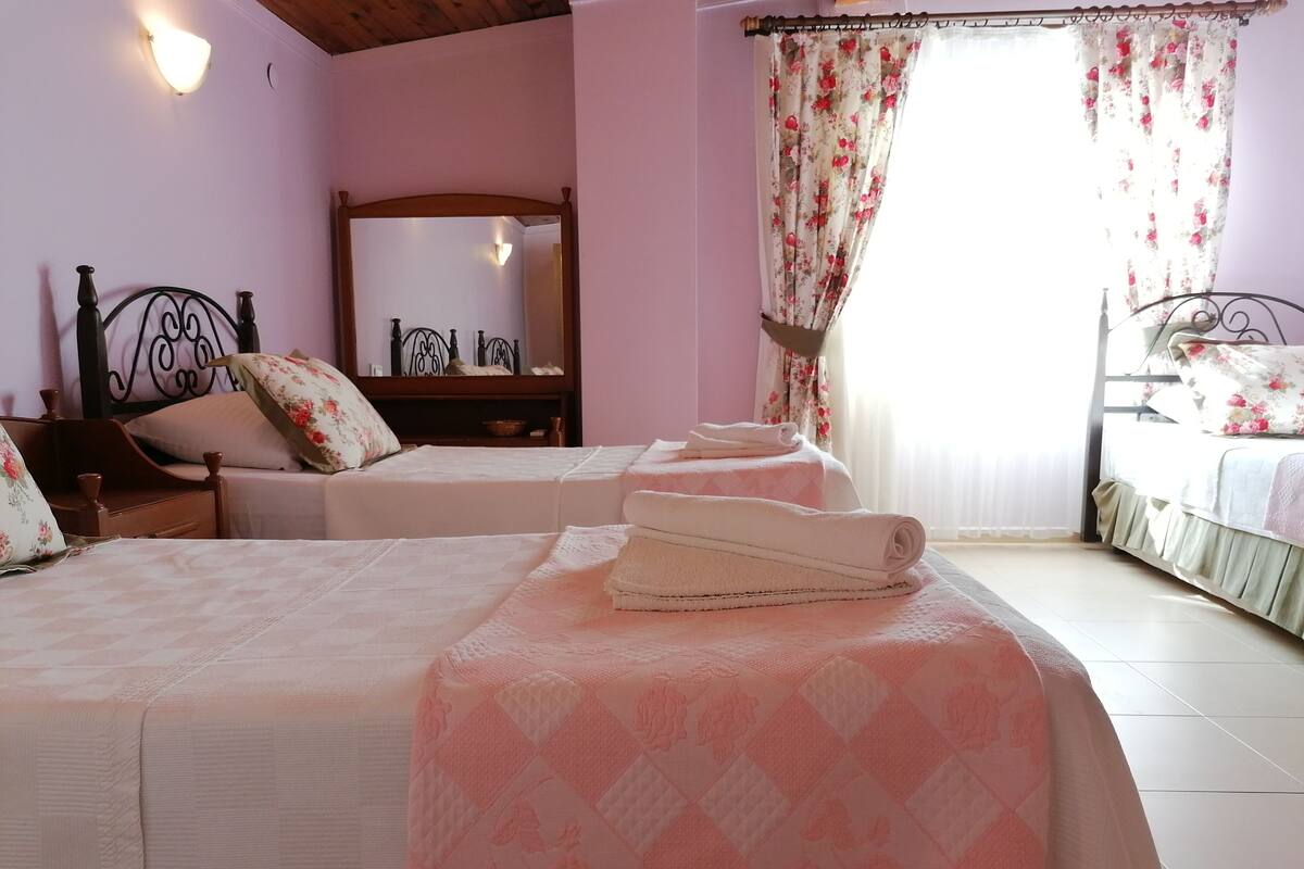 A bedroom with two beds, a wooden headboard, a mirror, and floral curtains.